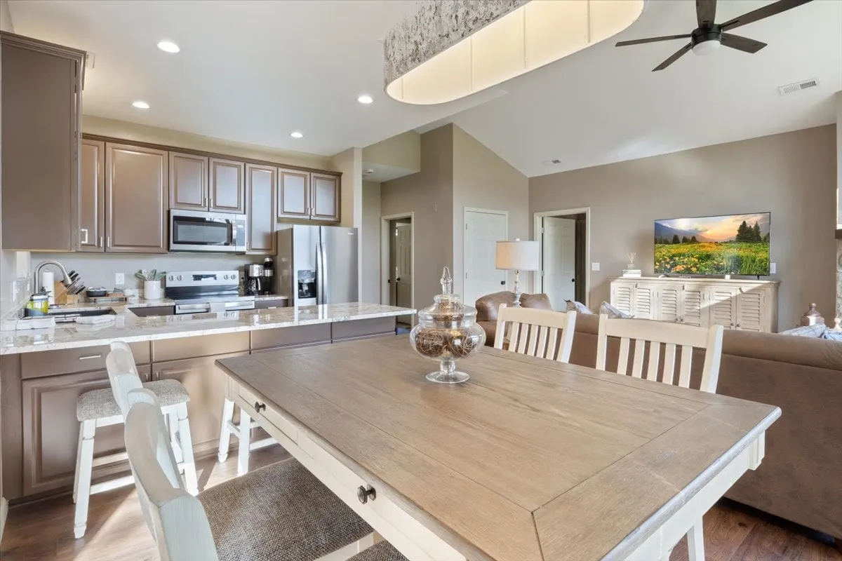 A bright kitchen with a central island, dining table, modern appliances, and a television displaying a landscape scene. The setup is ideal for cooking, entertaining, or relaxing with family and friends.