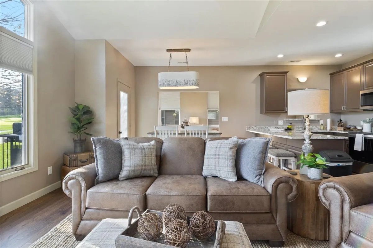 An open-plan living space with a comfortable sofa adorned with decorative pillows, a kitchen area visible in the background, and a dining table. The setting is ideal for socializing, sharing meals, and enjoying downtime with friends or family.