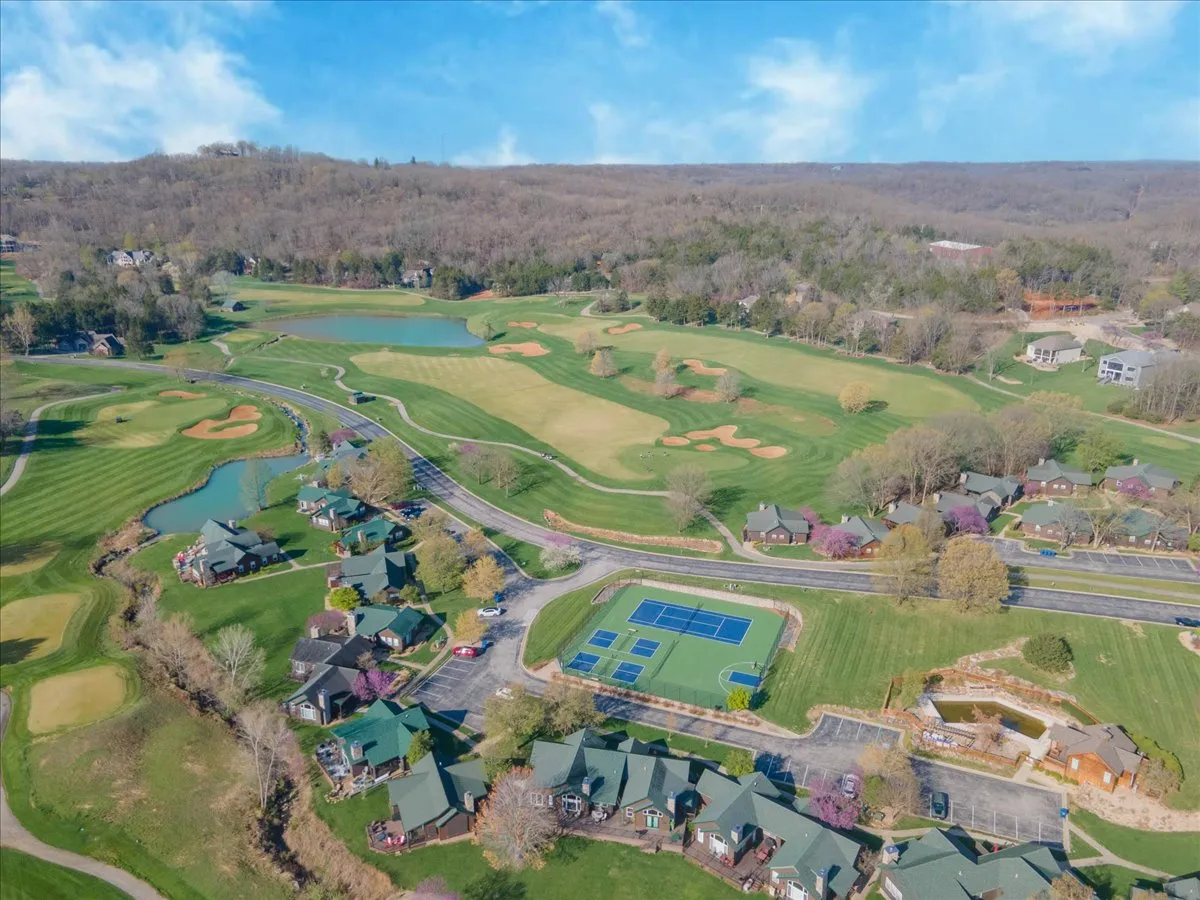 A sweeping exterior view of the golf course adjacent to residential homes, with the tennis courts and water features also visible. Activities like golfing and tennis are implied, with a tranquil mood set by sunset lighting. The scene embodies the lifestyle of living steps away from premier sporting and leisure options.