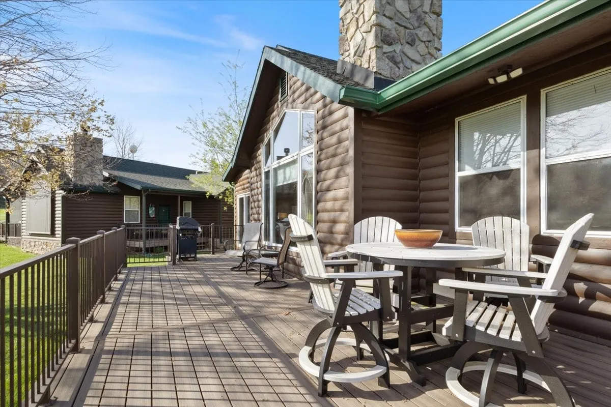 This image features a wooden deck furnished with a circular table and lounge chairs, set beside a stone chimney. The deck presents an inviting space for outdoor dining, social gatherings, and relaxation, with scenic views likely of the surrounding natural landscape.