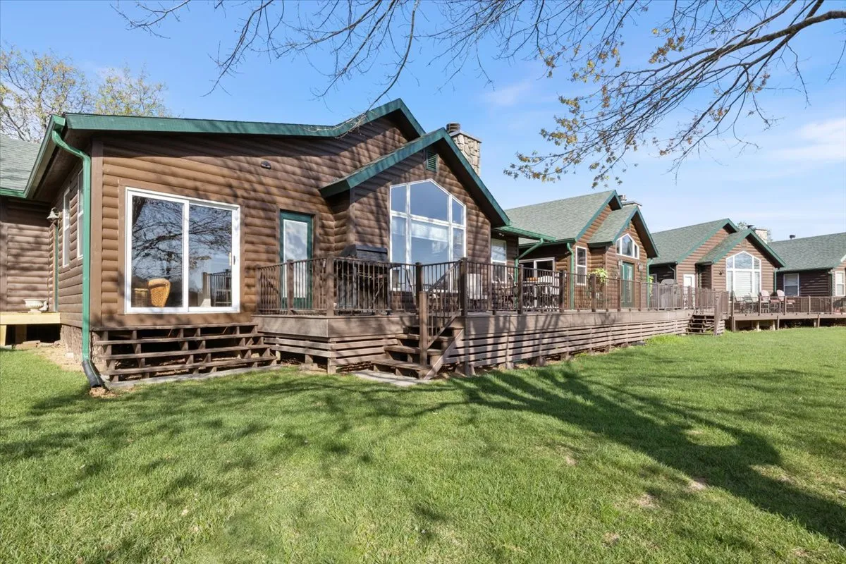 A welcoming exterior shot of a home features large windows, a spacious wooden deck, and a lush green lawn. The scene is set for outdoor gatherings, barbecues, and relaxed mornings with views of the surrounding landscape.