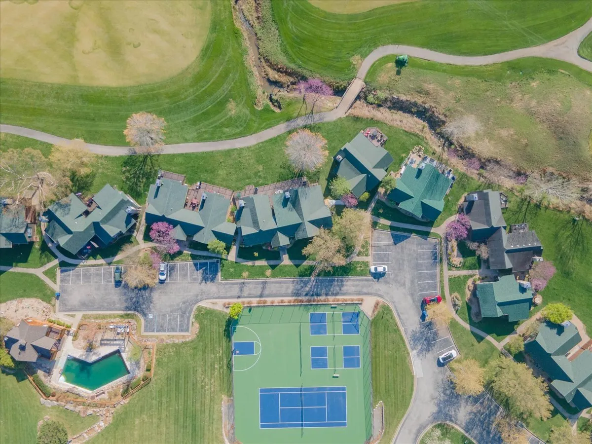 An exterior shot capturing the tennis courts and an outdoor swimming pool, set amid lush green lawns and a cluster of houses. The image is lively, evoking both active and relaxed moments—like sunny days filled with sports or evenings by the pool—while hinting at the broader communal experience.