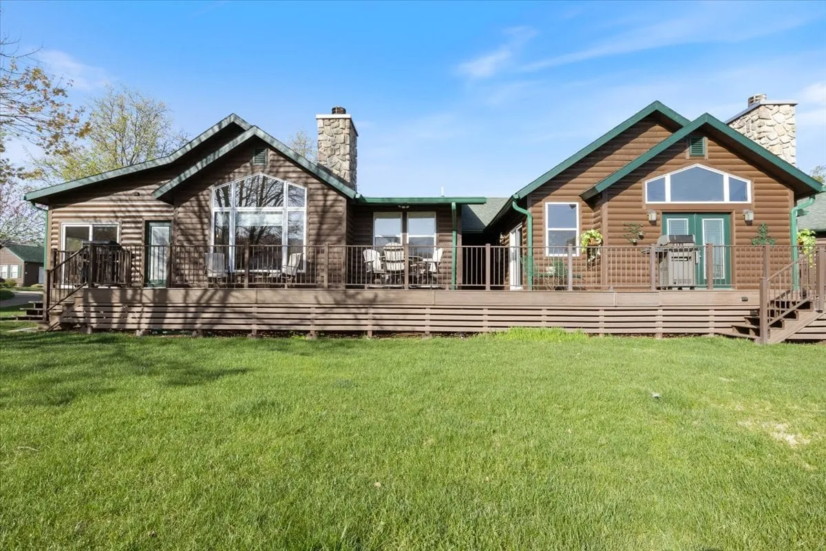A large exterior deck with outdoor dining furniture, a stone chimney, and expansive windows. The surrounding greenery adds to the welcoming vibe, making the deck ideal for gatherings or peaceful moments outside.