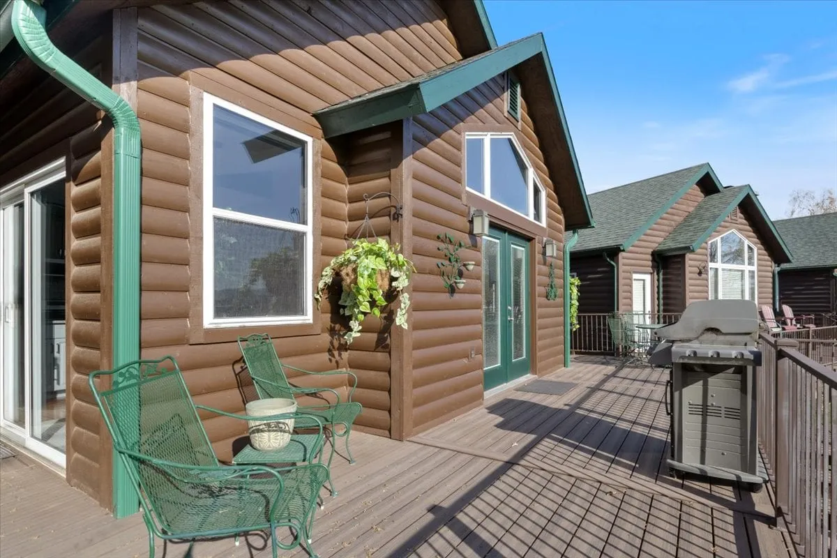 This image showcases the exterior of a log cabin with green accents and an outdoor seating area. The porch offers a welcoming atmosphere, ideal for relaxing and enjoying the outdoors, hinting at the cabin's immediate connection to nature and the golf course setting.