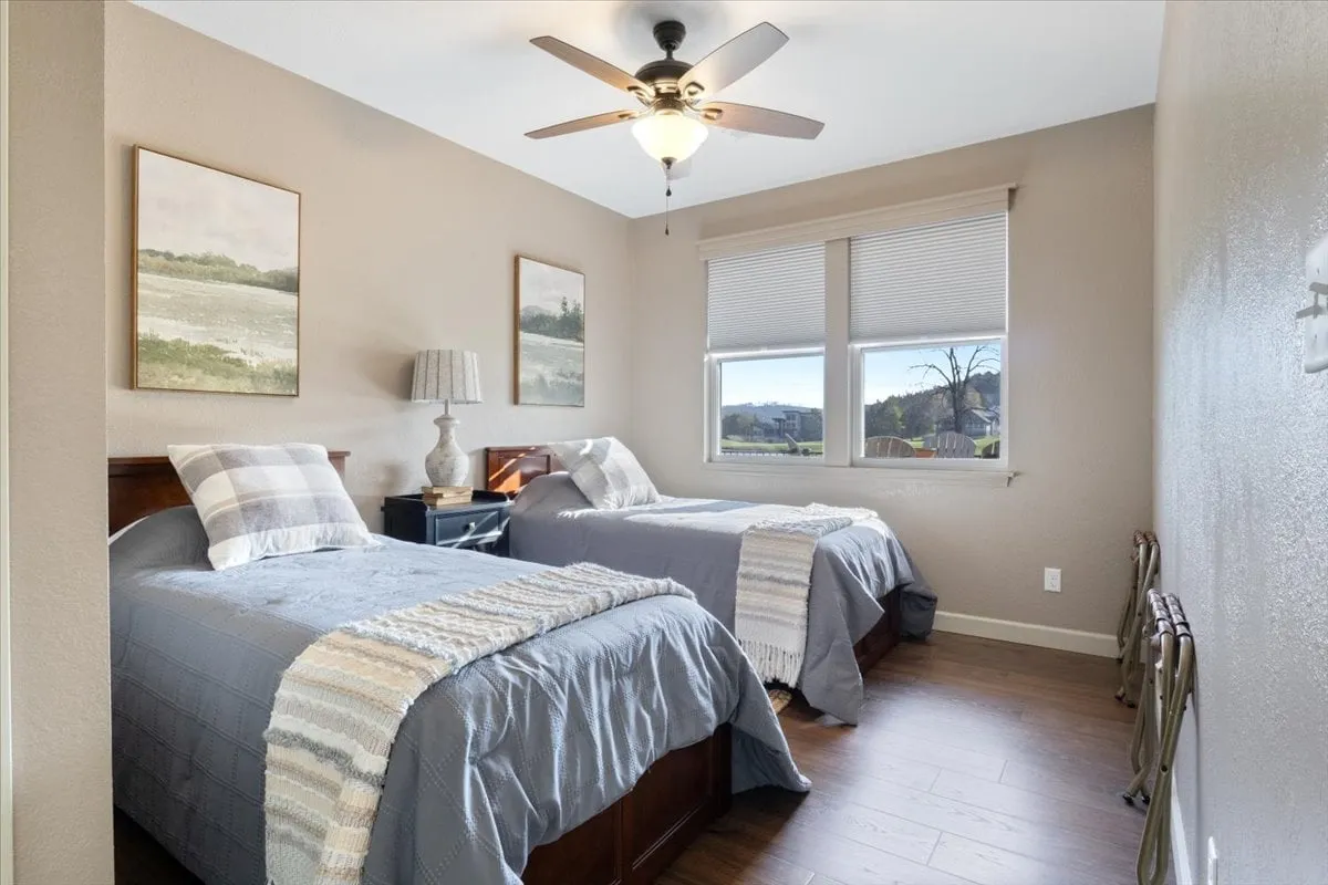 This image features a pair of neatly made twin beds with white and blue bedding, a lamp on a nightstand, and wall art above the beds. Natural light pours in from a window, creating a tranquil, cozy atmosphere ideal for unwinding after a day of adventure.
