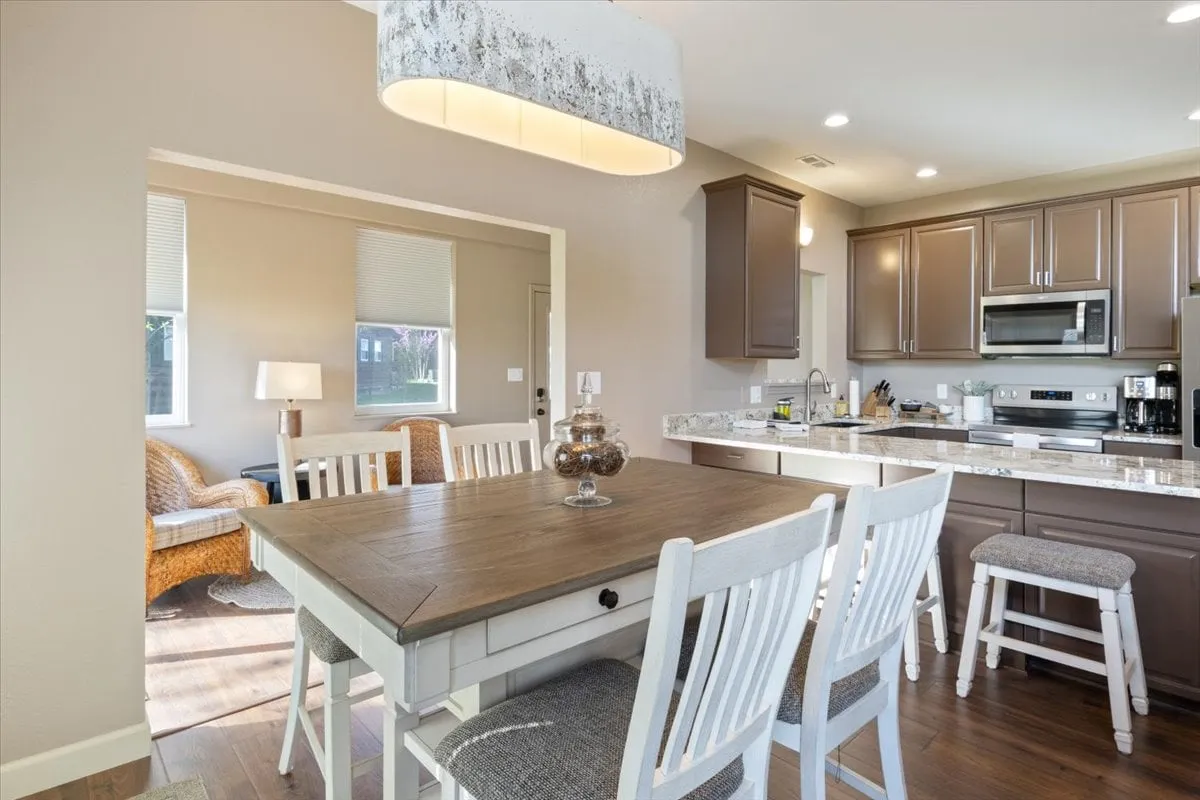 A spacious and inviting open-plan kitchen and dining area, featuring a kitchen island with bar stools, a large dining table, and a cozy seating area. Warm lighting and thoughtful design elements create an atmosphere perfect for meals, gatherings, and casual conversation.