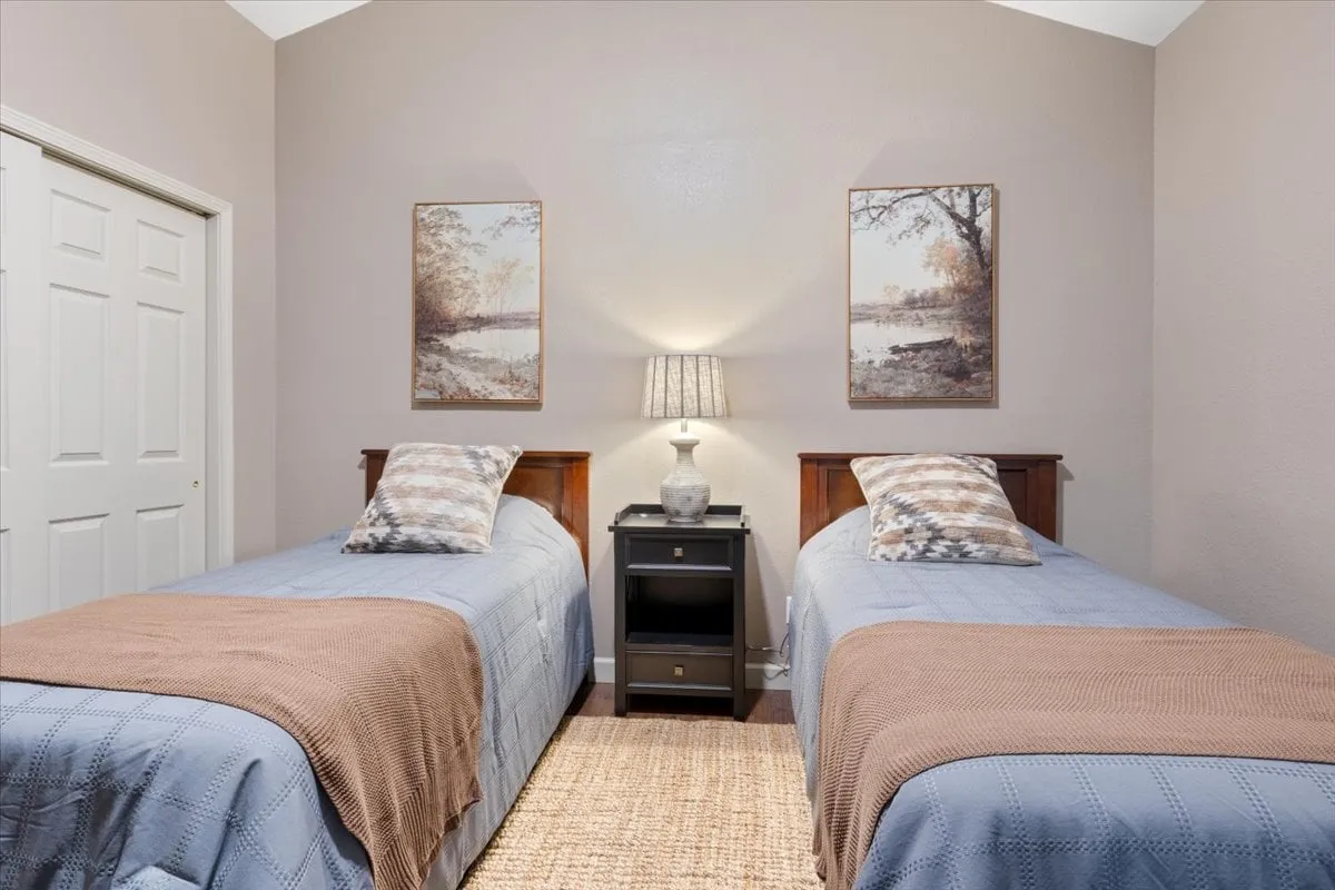 Two twin beds are dressed in stylish linens and flanked by a nightstand and lamp. The room includes decorative pillows and wall art, creating a friendly, welcoming space that encourages relaxation and late-night conversations.